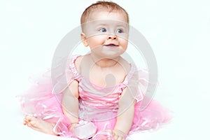 Adorable little baby girl in pink dress playing with her pink shoe