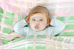 Adorable little baby girl after sleeping in bed. Calm peaceful child with a pacifier or dummy