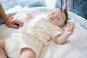 Adorable little baby lying on children rug looking up and playing with toys.