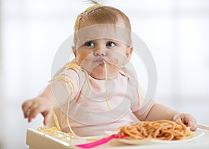 Adorable little baby one year eating pasta indoor. Funny toddler child with spaghetti. Cute kid and healthy food.