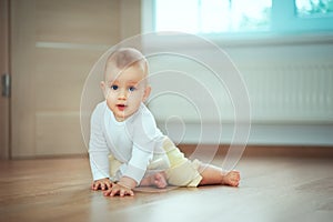 Adorable little baby sitting in bedroom on the floor with bottle with milk or water and laughing. Infant Childhood Kids People