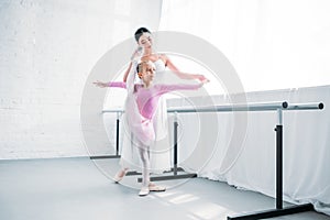 adorable little ballerina in pink tutu exercising with teacher