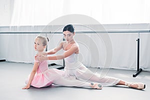 adorable little ballerina in pink tutu looking at camera while exercising with teacher