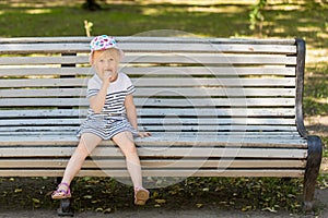 Adorable little blond girl sitting on a bench in a city park and eating cone ice-cream