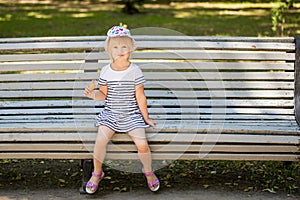 Adorable little blond girl sitting on a bench in a city park and eating cone ice-cream
