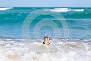 Adorable little blond kid boy having fun on ocean beach. Excited child playing with waves, swimming, splashing and happy