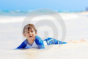 Adorable little blond kid boy having fun on tropical beach of Jamaica. Excited child playing and surfing in sun