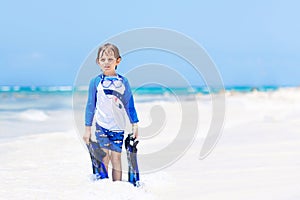 Adorable little blond kid boy having fun on tropical beach of Maldives. Excited child playing and surfing in sun
