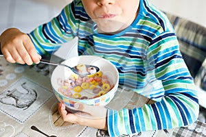 Adorable little blond school kid boy eating cereals with milk and berries for breakfast or lunch. Healthy eating for