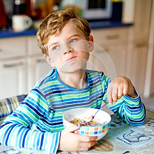 Adorable little blond school kid boy eating cereals with milk and berries for breakfast or lunch. Healthy eating for