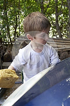 Adorable little blonde boy using a sponge to wash her parent`s car