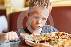 Adorable little boy eating pizza at a restaurant