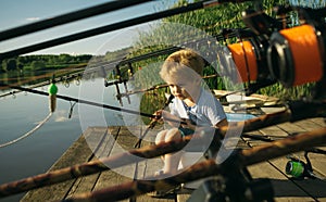 Adorable little boy fishing from wooden dock on lake