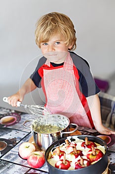 Adorable little boy helping and baking apple pie in home's kitchen