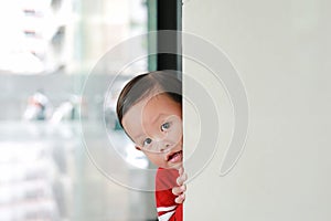 Adorable little boy hide behind a corner room. Baby playing peekaboo game indoor