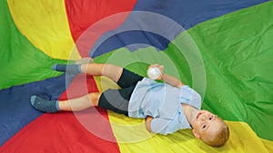 adorable little boy holding a ball and laying on the colorful piece at the nursery, full shot