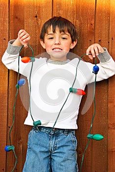Adorable little boy holding Christmas lights with funny smile.