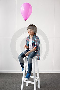 adorable little boy holding pink balloon while sitting in stool at birthday