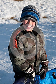 Adorable little boy holding sled smiling at camera wearing camo