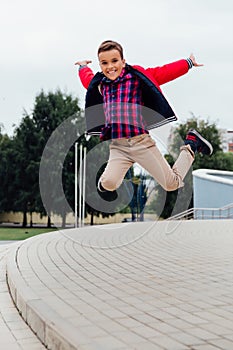 Adorable little boy jumping in the air on stairs in a city, wearing a brown leather jacket