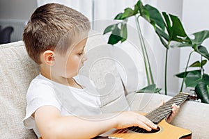 Adorable little boy learning to play acoustic guitar at home. Hobbies and entertainment for children at home