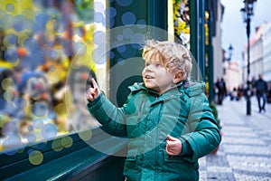 Adorable little boy looking through the window at Christmas decoration in the shop