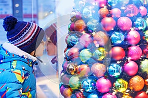 Adorable little boy looking through the window at Christmas decoration in the shop
