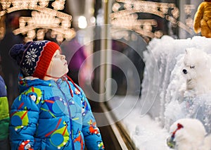 Adorable little boy looking through the window at Christmas decoration in the shop