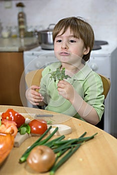 Adorable Little Boy Making Funny Face While Eating Parsley in the Kitchen