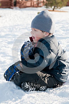 Adorable little boy in navy coat sitting in snow.