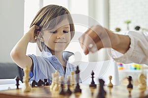 Adorable little boy playing chess with his mom at home. Cute child enjoying strategy board game with his parent indoors