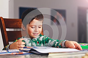 Adorable little boy reading book before going to sleep. Happy kid dressed in pajamas reads a story and amuses himself. Cute boy l