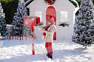 Adorable little boy with red hat and green glasses sending her letter to Santa, Christmas time