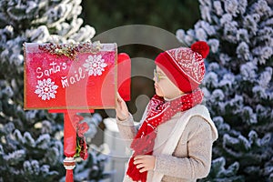 Adorable little boy with red hat and green glasses sending her letter to Santa, Christmas time