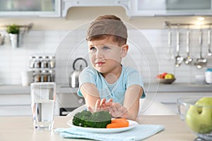 Adorable little boy refusing to eat vegetables at table