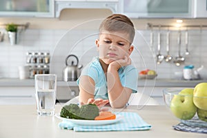 Adorable little boy refusing to eat vegetables at table