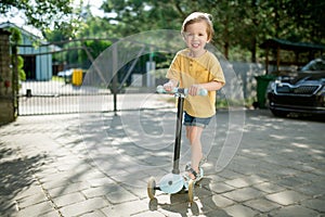 Adorable little boy riding his scooter in a back yard on sunny summer evening. Young child riding a roller