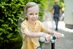 Adorable little boy riding his scooter in a back yard on sunny summer evening. Young child riding a roller