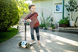 Adorable little boy riding his scooter in a back yard on sunny summer evening. Young child riding a roller