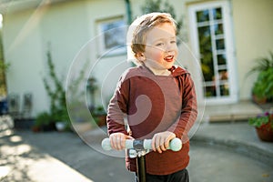 Adorable little boy riding his scooter in a back yard on sunny summer evening. Young child riding a roller