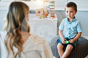 An adorable little boy sitting in his bedroom at home and talking to his mother. Happy male child bonding with his mom