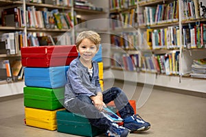 Adorable little boy, sitting in library, reading book and choosing what to lend, kid in book store