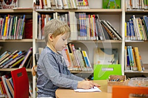 Adorable little boy, sitting in library, reading book and choosing what to lend, kid in book store