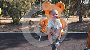 Adorable little boy on a swing with outstretched hands in slow motion, with a big smile on his face