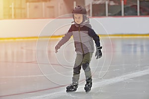 Adorable little boy in winter clothes with protections skating o