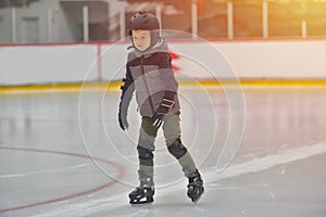 Adorable little boy in winter clothes with protections skating o