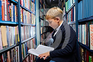 adorable little caucasian boy is sitting in a book store and read book