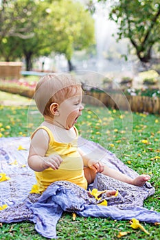 Adorable little Caucasian girl is playing with yellow flowers on a plaid at summer in park. Cute sleepy child