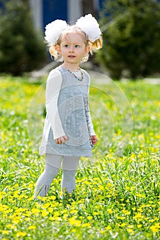 Adorable little child girl on grass on meadow. Summer green nature background.