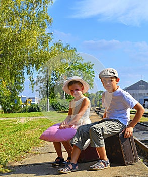 Adorable little children on a railway station, waiting for the train with vintage suitcases. Traveling, holiday and chilhood conce